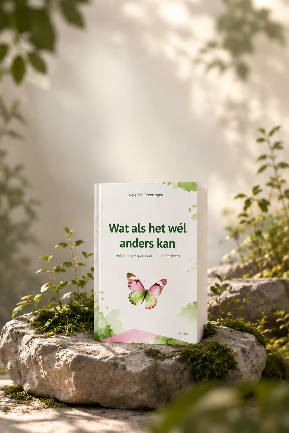 Het boek 'Wat als het wél anders kan' rechtop op een bemoste steen in zacht ochtendlicht